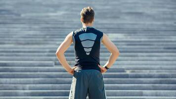 Training on stairs. Guy in sportswear, with fitness tracker at the beginning of the path and looking at steps, back, free space photo