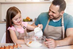 Happy Daddy And Little Daughter Making Dough Baking Cake For Father's Day Enjoying Cooking Together In Modern Kitchen At Home. Family Making Cookies And Pastry On Weekend photo