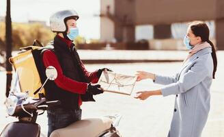 Safe Delivery Service. Courier In Protective Mask Delivering Package To Customer Standing With Scooter In Urban Area Outdoor. photo