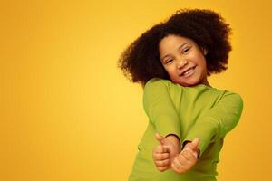 Everything is great. Positive cute little girl gesturing thumbs up and smiling at camera, yellow studio background with empty space photo