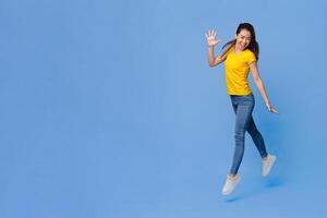 Joy Of Youth. Cheerful Asian Girl Jumping In The Air Over Purple Studio Background, Full-Length Shot With Copy Space photo