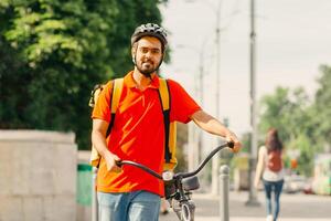 Traffic light and pedestrian crossing in city. Friendly young man courier in helmet with big yellow bag and bicycle, walks along the road in city, copy space photo