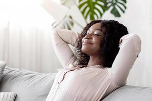 Weekend At Home. Relaxed Black Woman Leaning Back On Couch With Closed Eyes, Resting On Comfortable Sofa In Cozy Living Room With Hands Behind Head, Enjoying Spending Day Off, Copy Space photo