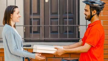 Pizza delivery service. Smiling courier in helmet with bicycle gives box for client at house at entrance, side view, free space photo