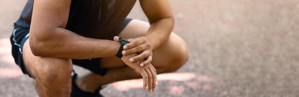 Closeup view of young black jogger checking smartwatch during his morning workout photo
