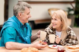 Smiling mature man and his wife enjoying morning coffee with jam toasts at campground photo