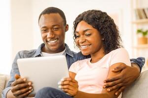 Closeup of smiling young african man and woman using digital tablet while resting at home photo