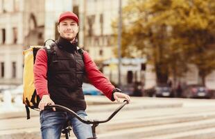 Courier Man On Bike Standing With Bag Delivering Food In City, Smiling To Camera. Free Space For Text photo