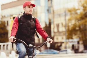 Delivery Guy With Delivering Backpack Posing With Bike In Urban Area Outdoors. Courier Service Concept. Blank Space For Text photo