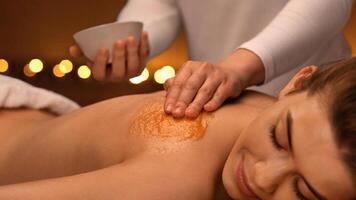Spa therapist applying exfoliating body mask on sleeping woman back at luxury spa decorated with candles and aroma plates, body care concept. Lady having skin scrubbing procedure at spa salon photo
