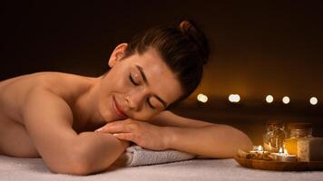 Side view of tranquil young woman spending day at spa salon decorated with candles, getting aroma session with relaxing full body massage, panorama with copy space. Spa, massage, relaxation concept photo