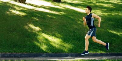 Sportsman in park. Guy in sportswear with sneakers and fitness tracker runs at track, side view, free space photo