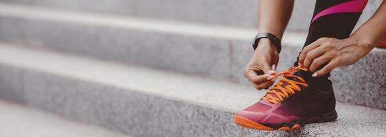 Morning run in city. African american girl with fitness tracker ties shoelaces on fashionable sneakers, close up, panorama, free space photo