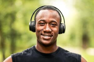 Closeup portrait of smiling african sportsman over blurred park background, listening to music while running photo