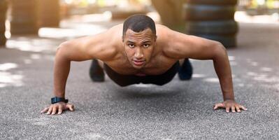 Strong black guy doing push ups or plank exercise after running at park in morning, panorama photo