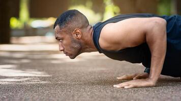 Side view of muscular black guy working out outdoors, doing push up exercises at park. Panorama photo