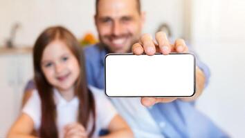 Father And Daughter Showing Smartphone Blank Screen To Camera Sitting In Kitchen At Home. Mobile App. Shallow Depth, Selective Focus photo