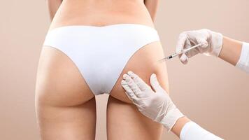 Sculptra butt lifting concept. Slim woman having hip injection at beauty salon, closeup. Plastic surgeon making injection at butt area for unrecognizable lady, grey studio background, back view photo
