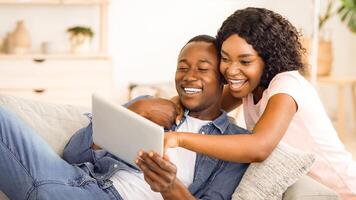 Black couple having fun together at home, using digital tablet, empty space photo