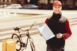 Courier Job. Delivery Guy Holding Folder With Paper Smiling To Camera Standing With Bike In City. Blank Space photo