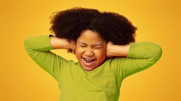 Annoyed little african girl covering ears with hands, doesn't want to hear or know something, emotionally reacting to arguing, yellow background photo