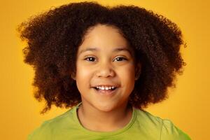 Portrait Of Adorable Curly Little Black Girl Smiling At Camera While Posing Over Yellow Background In Studio, Closeup photo