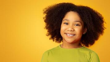 Portrait of pretty little african american girl smiling and looking at camera while posing over yellow background in studio, free space photo