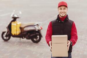 Parcel Delivery. Cheerful Courier Holding Boxes Smiling To Camera Standing Near Motorbike In City. Empty Space For Text photo