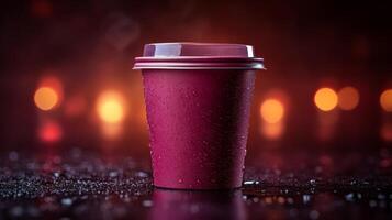 A warm cup of coffee rests on a shiny surface, droplets forming on its exterior. The background is softly illuminated with blurred lights, creating a cozy, inviting atmosphere in the evening. photo