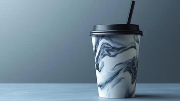 A marbled cup with a black lid and straw rests on a smooth gray surface. The design features swirling black and white patterns, creating a stylish appearance. photo