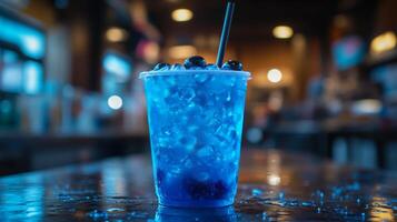 A vibrant blue drink filled with ice and fresh blueberries sits on a wooden table. The ambiance suggests a bustling evening atmosphere with soft lighting in the background. photo
