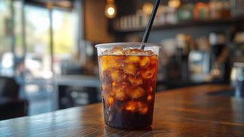 A clear cup filled with iced coffee sits on a wooden table in a modern cafe. The setting features warm lighting and comfortable seating, inviting customers to relax. photo