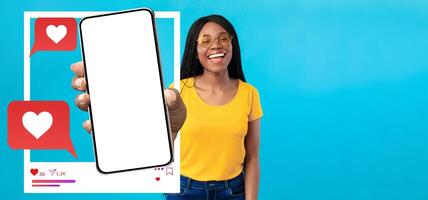 A cheerful influencer holds up a smartphone against a bright blue background. The device features empty social media icons, inviting engagement. She's smiling and ready to connect online. photo