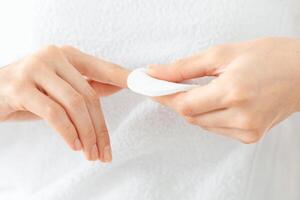 Unrecognizable woman removing lacquer from manicured nails with white cotton pad and acetone. Closeup of lady using nail polisher remover and cotton pad, making manicure at home, cropped photo