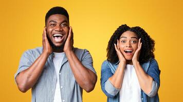 Two friends express delight and surprise, showing excitement with wide smiles and hands on their faces against a bright yellow background, capturing a moment of shared joy. photo