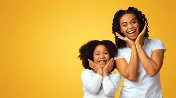 Cheerful black mom and daughter having fun together, making funny poses and gestures and sincerely laughing over pink background, empty space photo