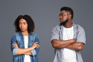 Two individuals face away from each other, showing crossed arms and a lack of eye contact. This conveys tension and unresolved emotions in a neutral studio setting. photo