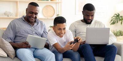 A family of three sits together on a couch, with two adults engaging with tablets and a child happily playing games, creating a lively atmosphere at home. photo