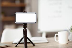 Teaching online from her well-organized desk. Smartphone with blank screen on a tripod to facilitate remote learning, demonstrating modern e-learning practices. photo