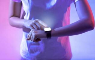 A person is using a smartwatch, tapping the screen while illuminated by vibrant lights. The setting suggests a modern living space, creating a tech-focused atmosphere. photo