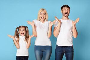 Joyful Surprise. Happy Parents And Daughter Screaming In Delight Over Blue Background In Studio. photo