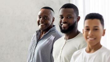 A joyful moment is captured with three men from different generations smiling warmly. They are standing side by side in a well-lit area, showcasing a connection and happiness. photo