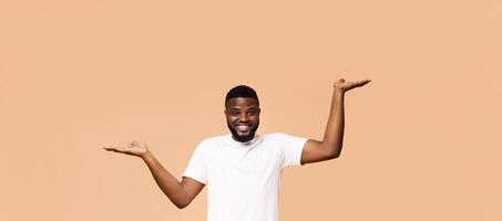 Make right choice. Positive african american man comparing variants, making scales with his empty hands, orange studio background,free space photo