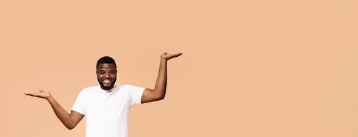 Make right choice. Positive african american man comparing variants, making scales with his empty hands, orange studio background,free space photo