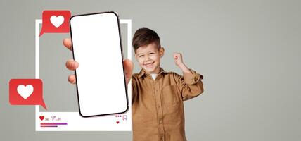A child happily displays a smartphone with an empty screen while raising a fist in excitement. The background is plain, emphasizing the mockup for social media applications and interactions. photo