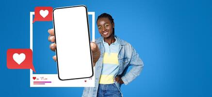 An influencer holds a blank smartphone displaying social media icons while smiling. She stands against a vibrant blue background, emphasizing her connection to online chatting and engagement. photo