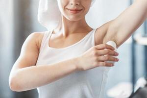 Millennial Caucasian girl using roller deodorant after shower near mirror at bathroom photo