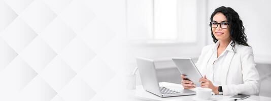 Busy Woman. Confident latin lady using laptop computer, holding digital tablet, looking at camera, copy space photo