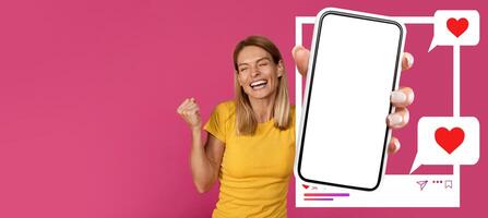 A smiling influencer stands against a bright pink background, holding a smartphone displaying a mockup screen. She seems excited about her online interactions, showcasing enthusiasm for social media. photo