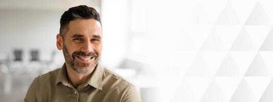 A middle aged businessman with a beard is smiling while seated in a modern office. Natural light floods the space, enhancing the professional atmosphere and his entrepreneurial spirit, copy space photo